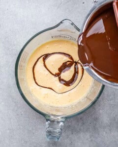 Melted chocolate being poured into the whipped egg yolk and sugar mixture in a glass bowl.