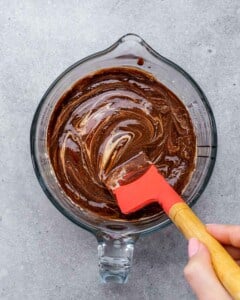 Thick chocolate mixture in a glass bowl being folded with a red spatula.