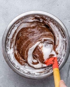 Mixing bowl with chocolate mixture being gently folded with a red spatula to combine egg whites and chocolate.