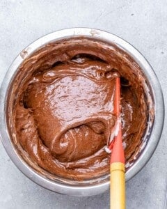 Mixing bowl filled with smooth chocolate soufflé batter being stirred with a red spatula.