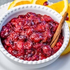 A white bowl filled with cranberry sauce with a cinnamon stick in bowl.