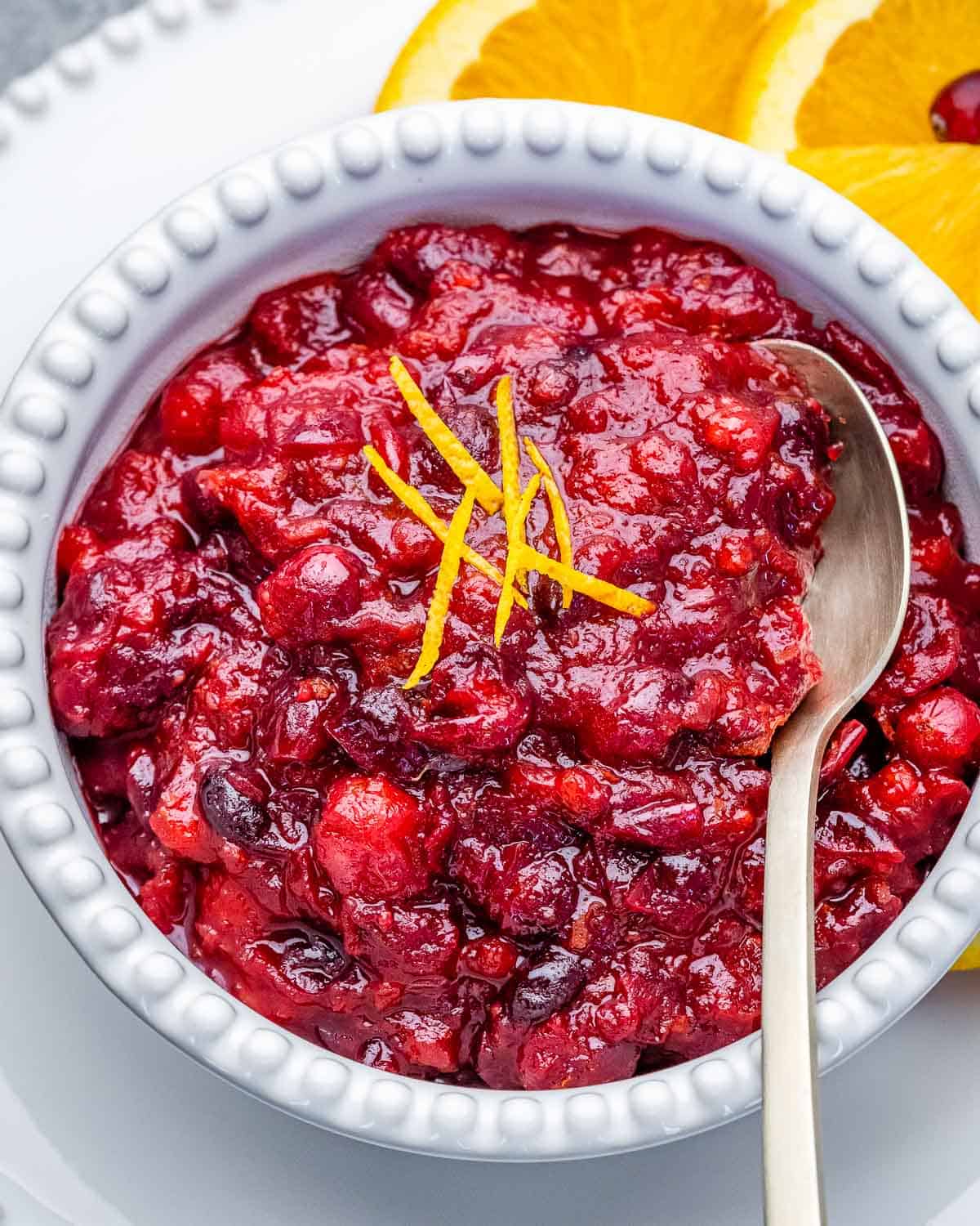 A white bowl filled with cranberry sauce with a cinnamon stick in bowl.