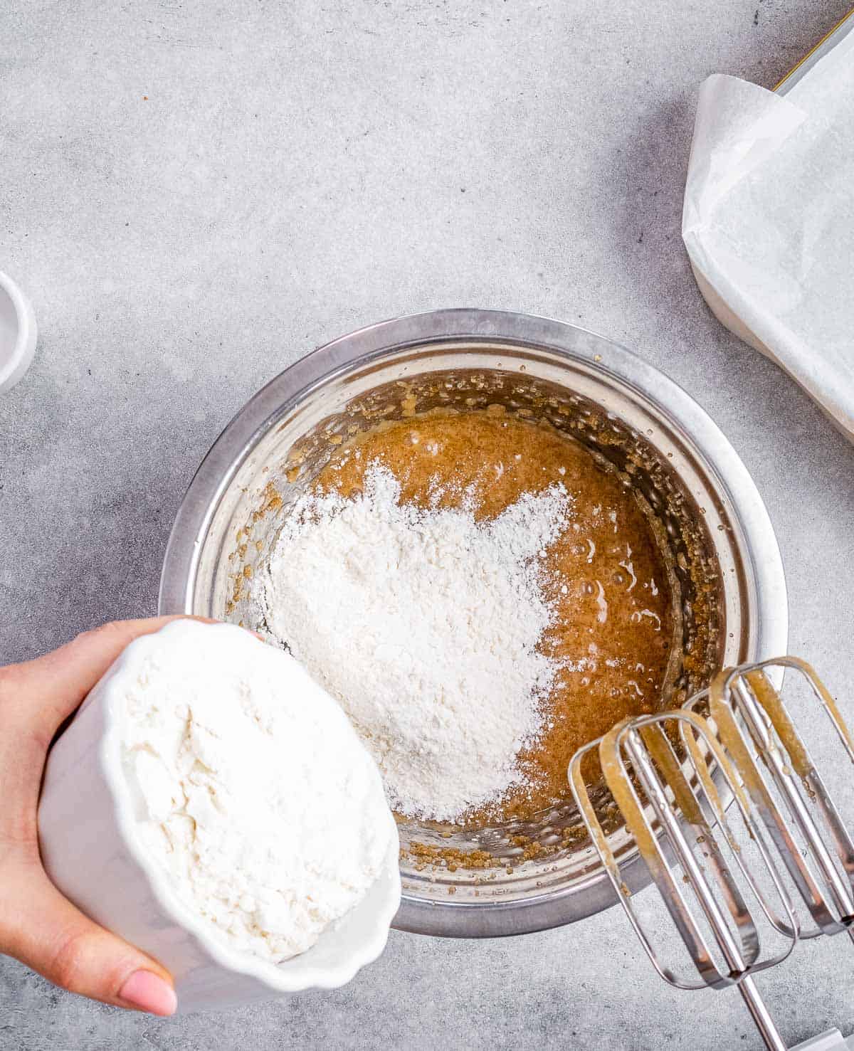 flour being poured into egg batter mixture in a bowl.