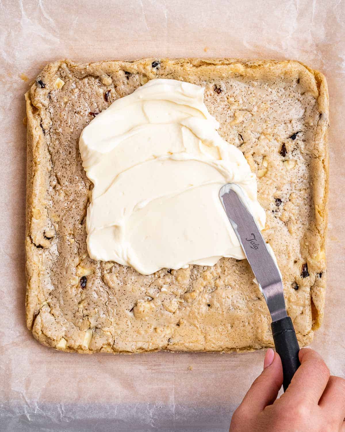 cream cheese topping being added over the cookies base.