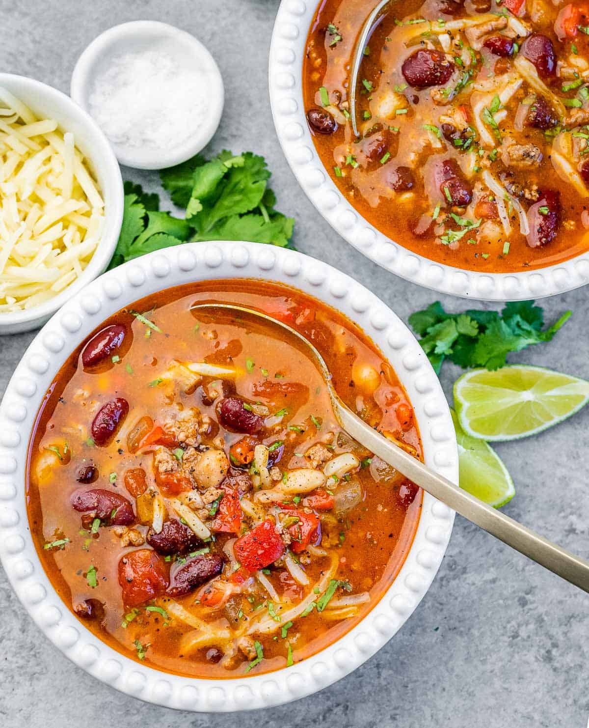 Two white bowls of chili with spoon in the bowl.