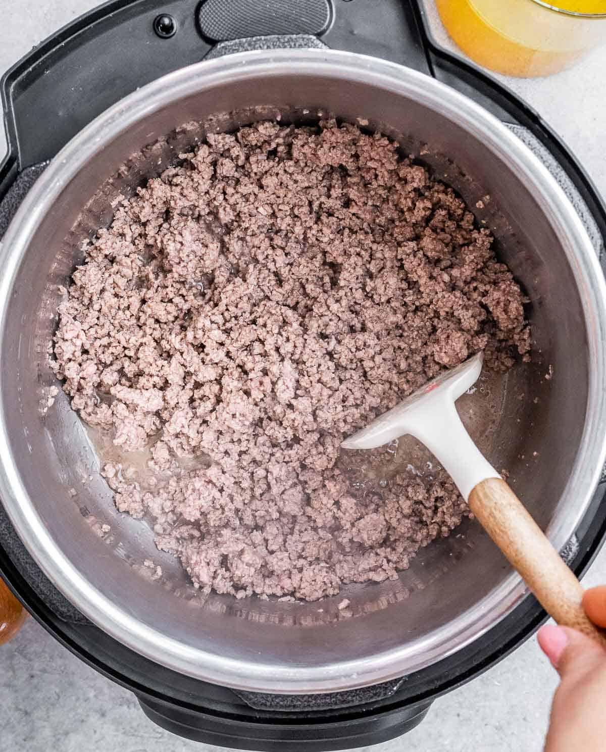 A white spatula stirring a pot with cooked ground beef.