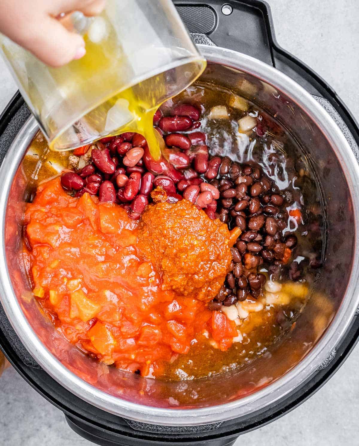 Pouring liquid into a pot filled with beans and tomatoes.