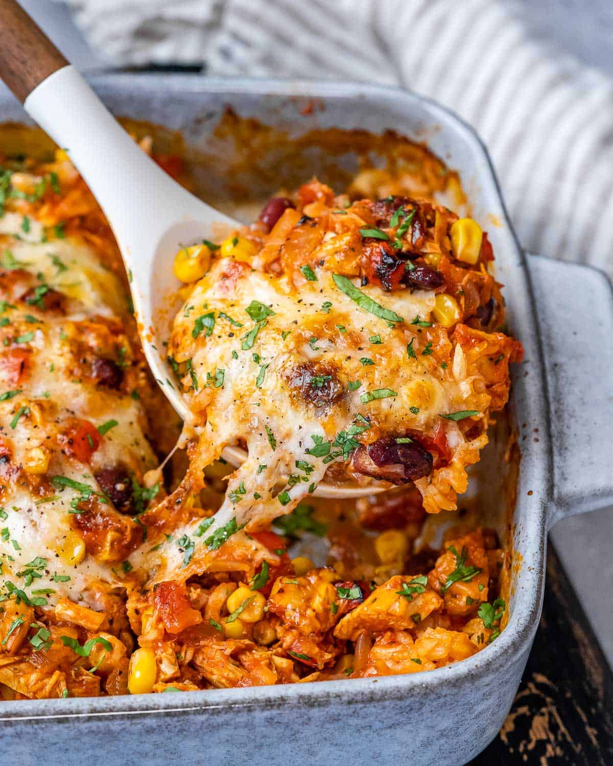 cheesy Mexican chicken casserole in white dish with spoon