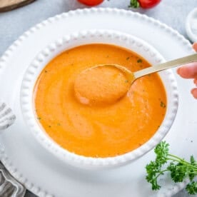 creamy orange looking tomato soup in a white round bowl with spoonful of soup.