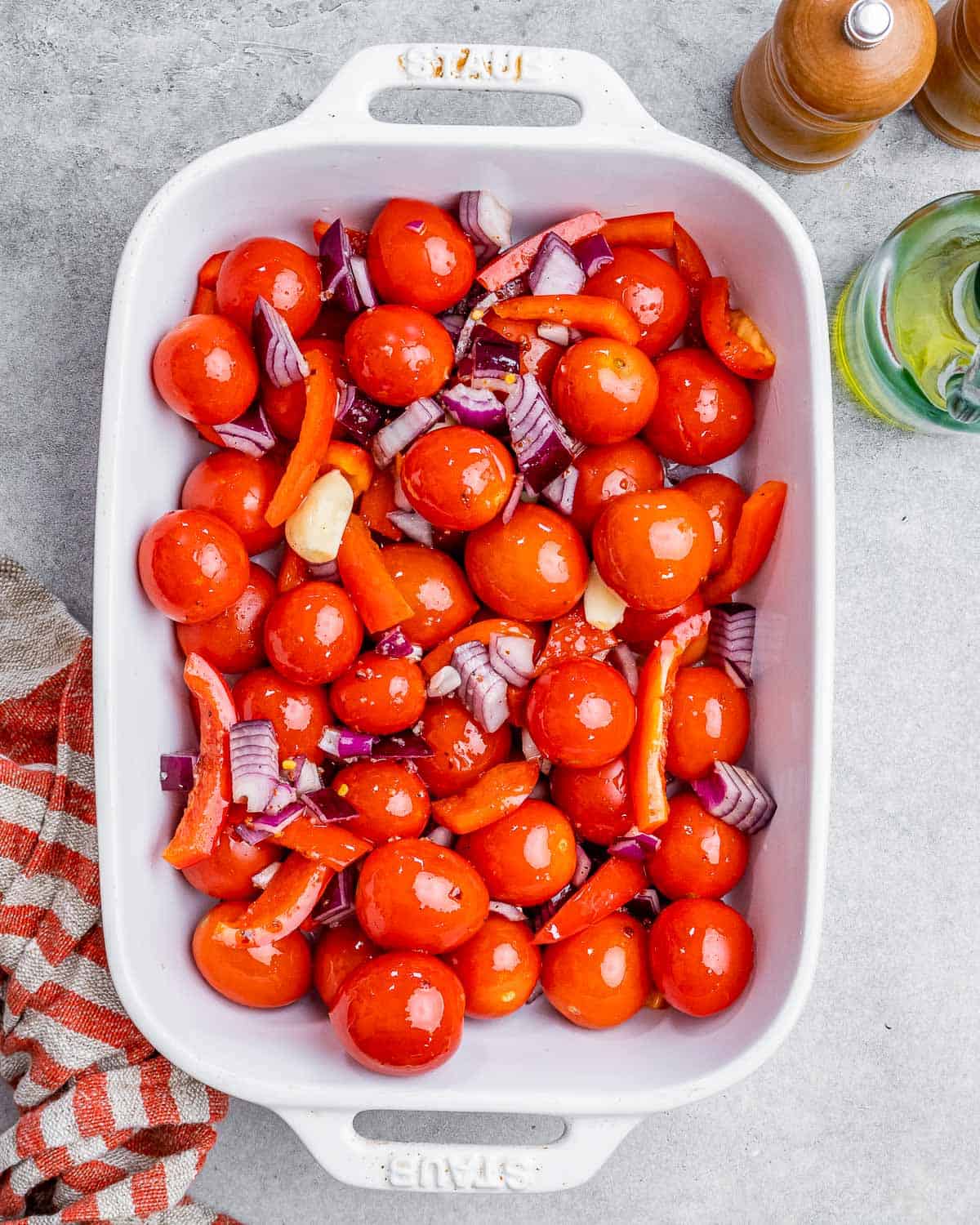 Tomatoes, onions, and peppers mixed with herbs in a white baking dish.