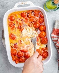 Fork mashing the cheese and tomatoes in a baking dish.