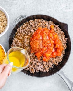 pouring tomatoes and broth into cooked ground beef in pan