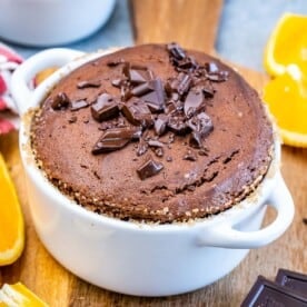Baked Chocolate Soufflé in a white ramekin, sprinkled with chopped chocolate pieces and placed beside fresh orange slices.