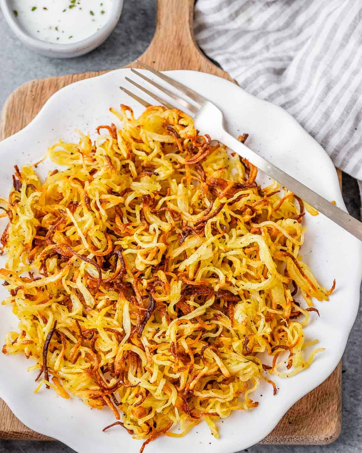 Air fried hash browns on a white plate with a fork and striped napkin.