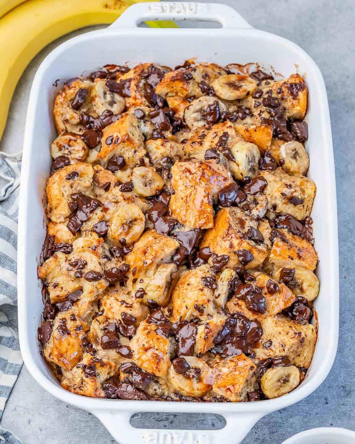 a white baking dish with baked banana bread pudding with chocolate chips and sliced bananas.