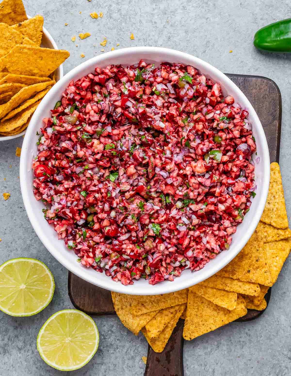 A white bowl filled with cranberry salsa and tortilla chips around the bowl.