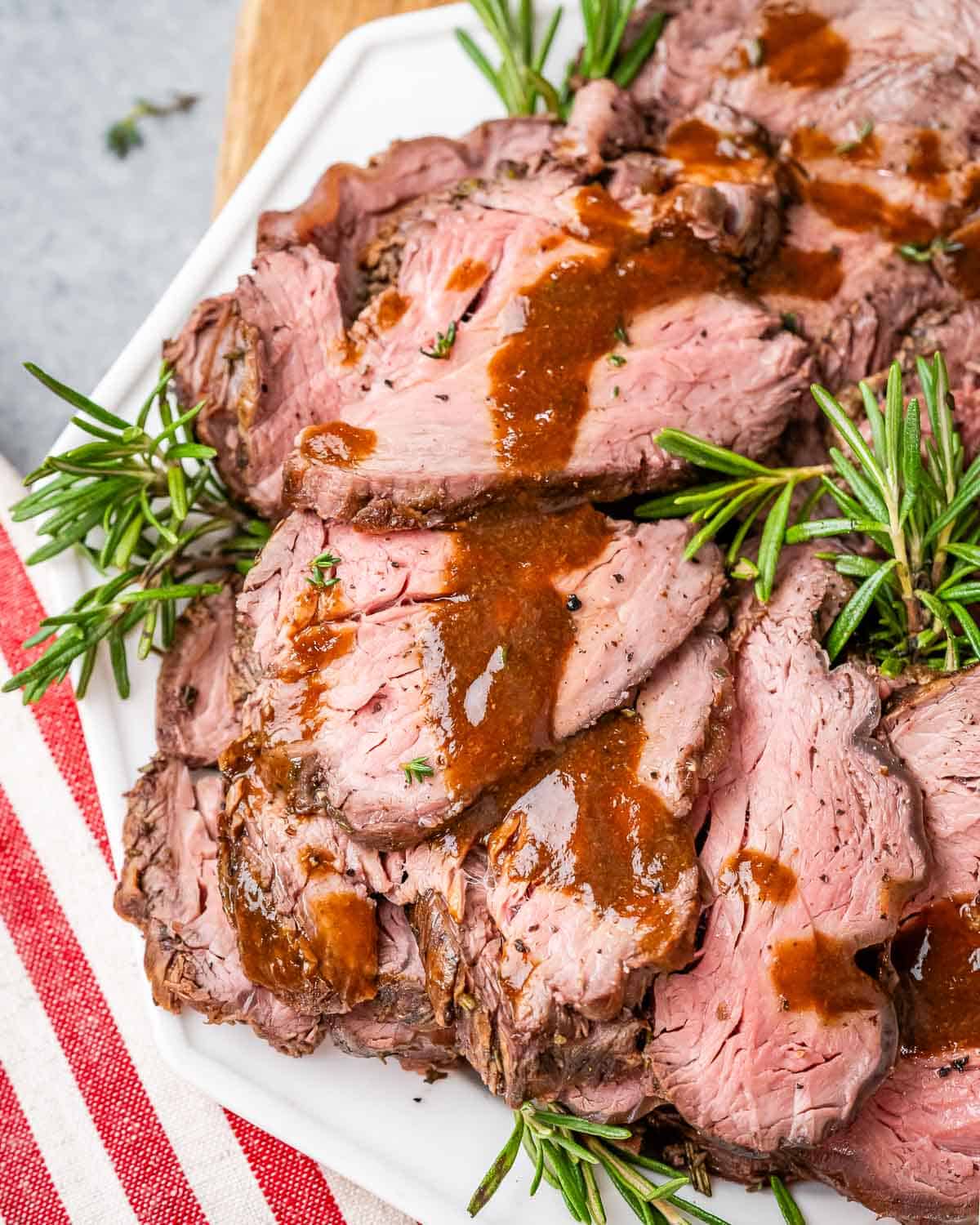 Sliced roast beef drizzled with rich brown gravy, served with rosemary for a simple, elegant presentation.