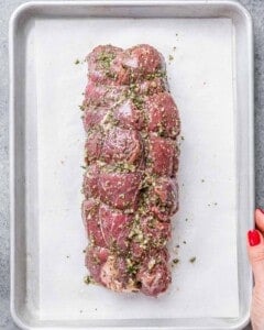 Raw tied beef coated in garlic, herbs, and oil, ready to roast.