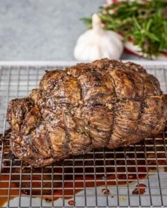 Whole roast beef resting on a rack after coming out of the oven, deep brown crust on top.