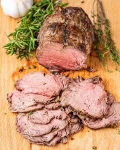 Perfectly roasted beef on a cutting board, juicy slices showing a pink center.