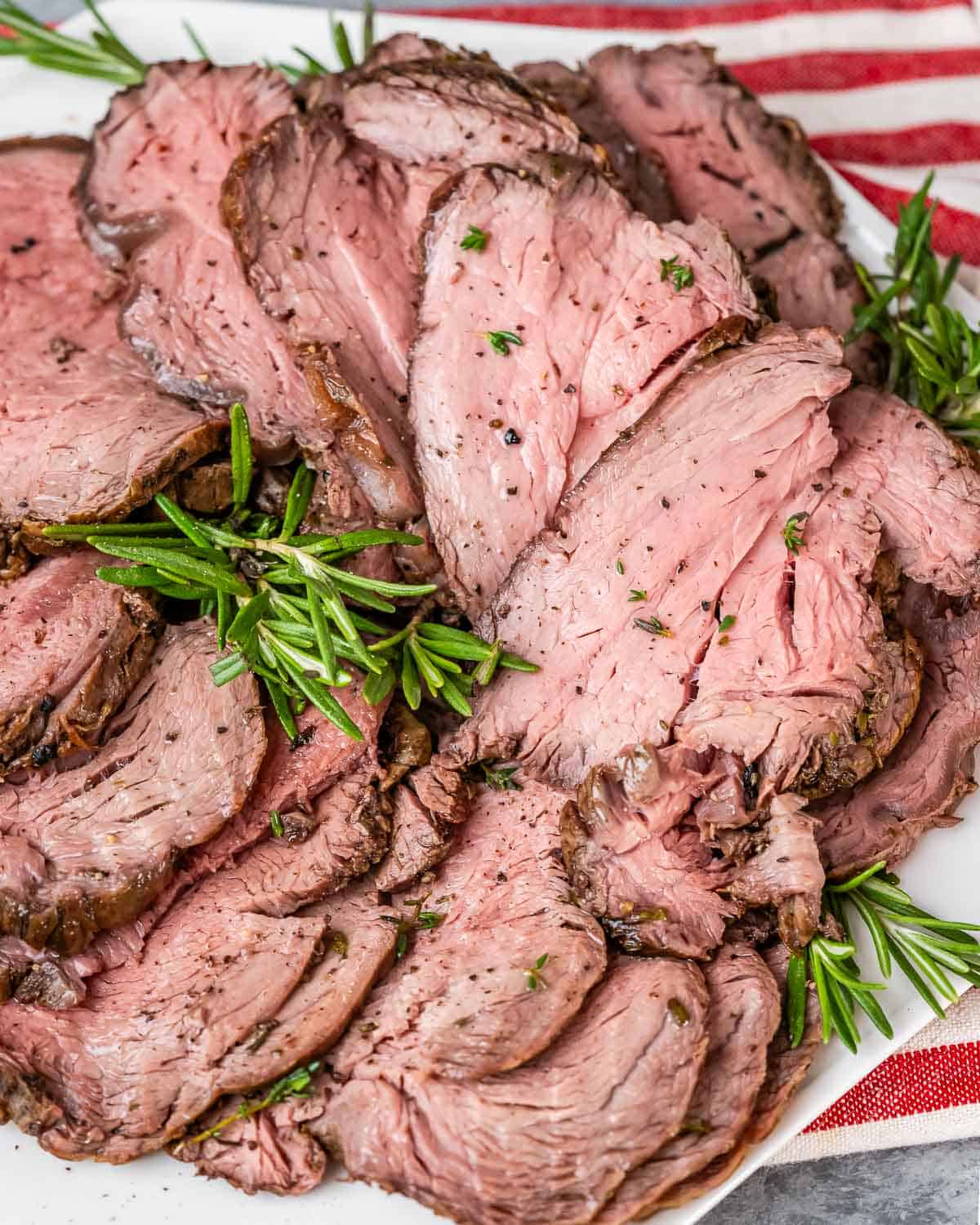 Sliced roast beef arranged on a plate with fresh rosemary sprigs.