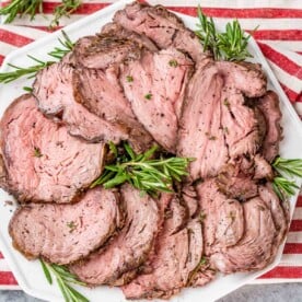 Tender slices of roast beef arranged with rosemary on a white plate.