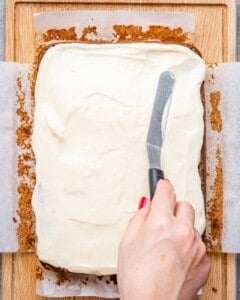 vanilla frosting being spread over gingerbread cake.