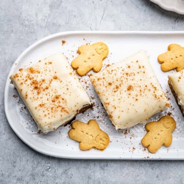 Two gingerbread cake squares on a plate with frosting over it.