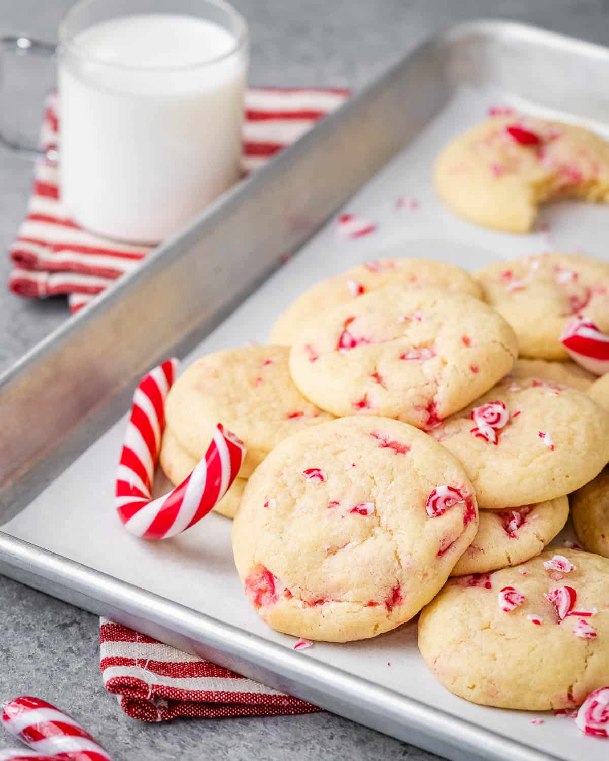 white sugar cookies with peppermint on a sheet pan and a candy cane next to the cookies.