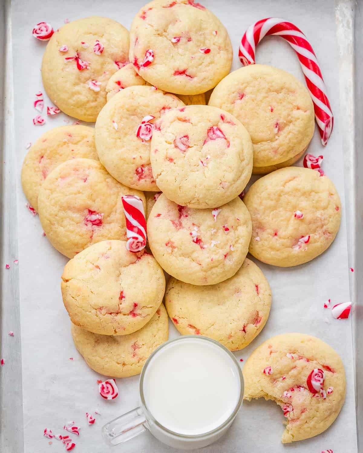 a sheet pan with many peppermint cookies and a jar of milk next to the cookies.