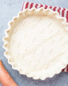 Raw pie crust in a dish with fork holes pricked into the bottom, ready for filling.