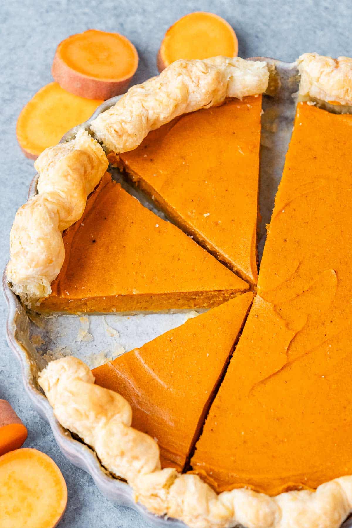 Sweet potato pie with several slices cut out, showing the smooth orange filling and crisp, golden crust.