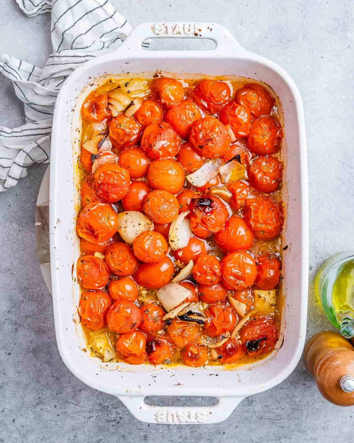 Roasted tomatoes and onions in a white casserole dish.