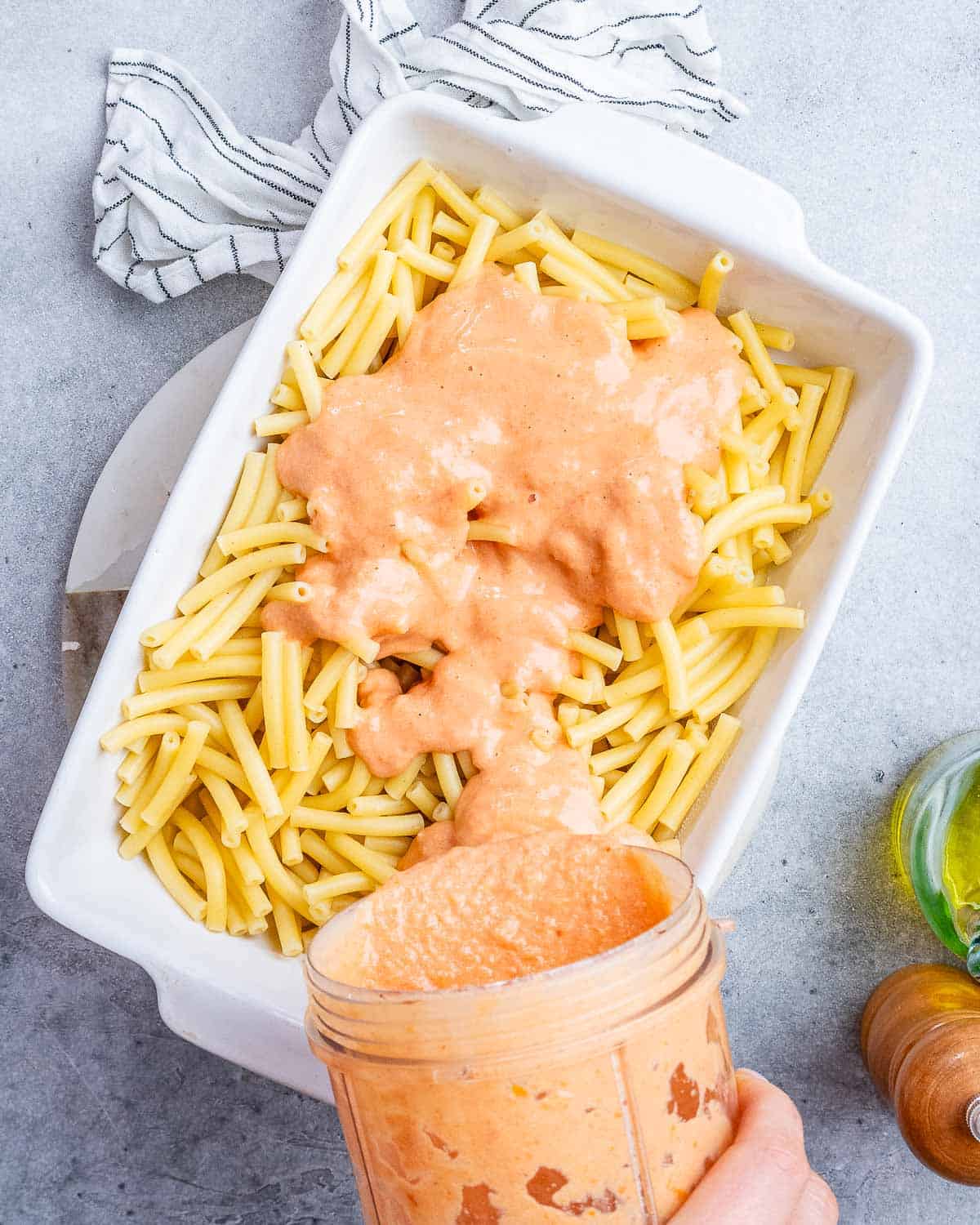 Pouring sauce over pasta in a white casserole dish.