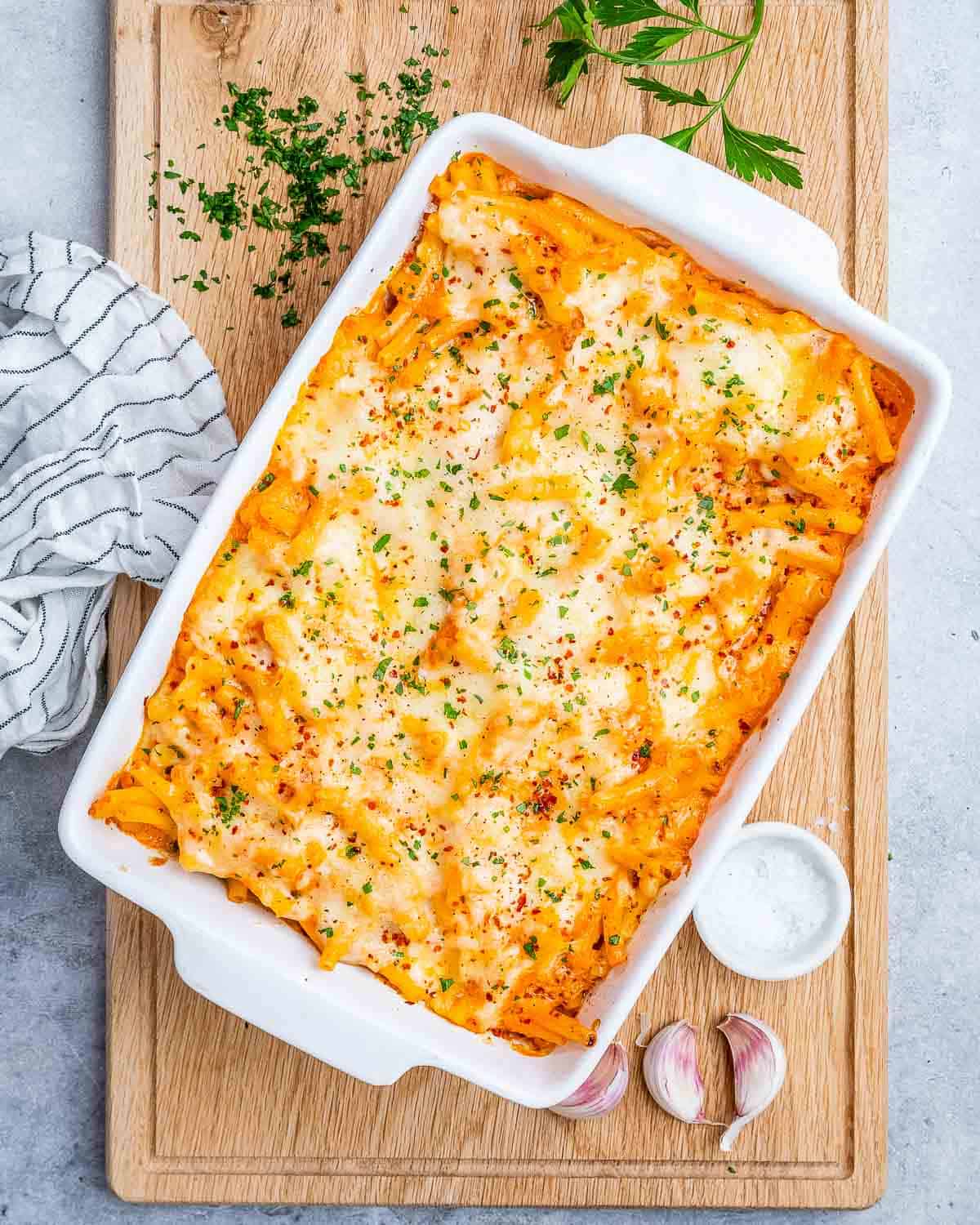 a white baking dish with baked ziti pasta sitting on a brown cutting board.