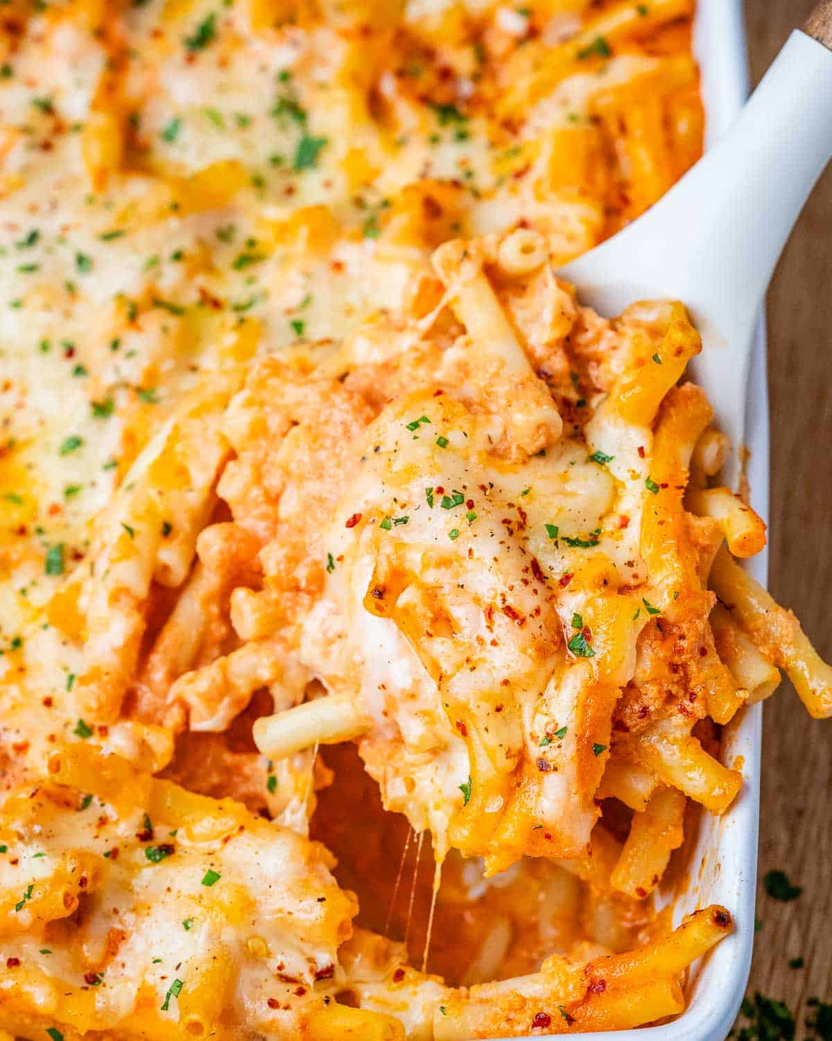 White baking dish filled with cheesy pasta being lifted by a spoon.