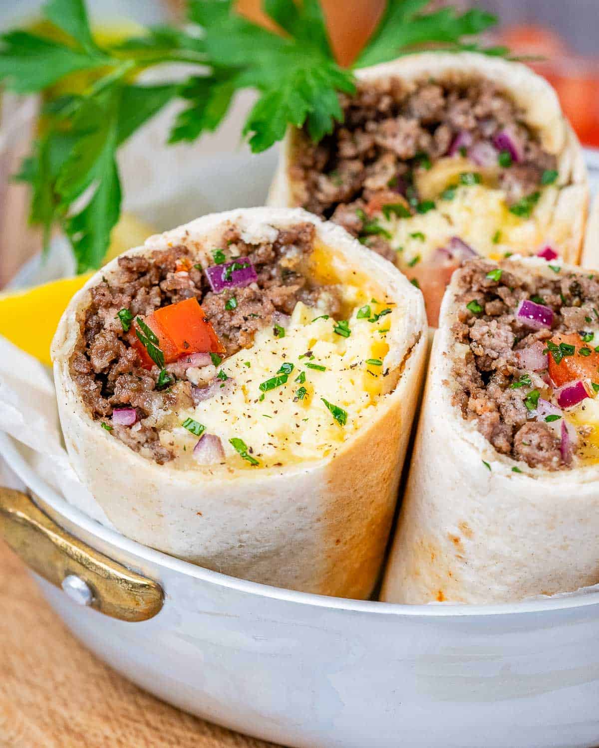 Three halves of a breakfast burrito standing up to show the ingredients on a white plate.