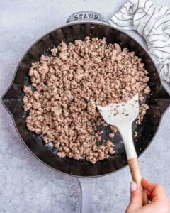 Ground sausage in a cast iron skillet stirred by a spatula.