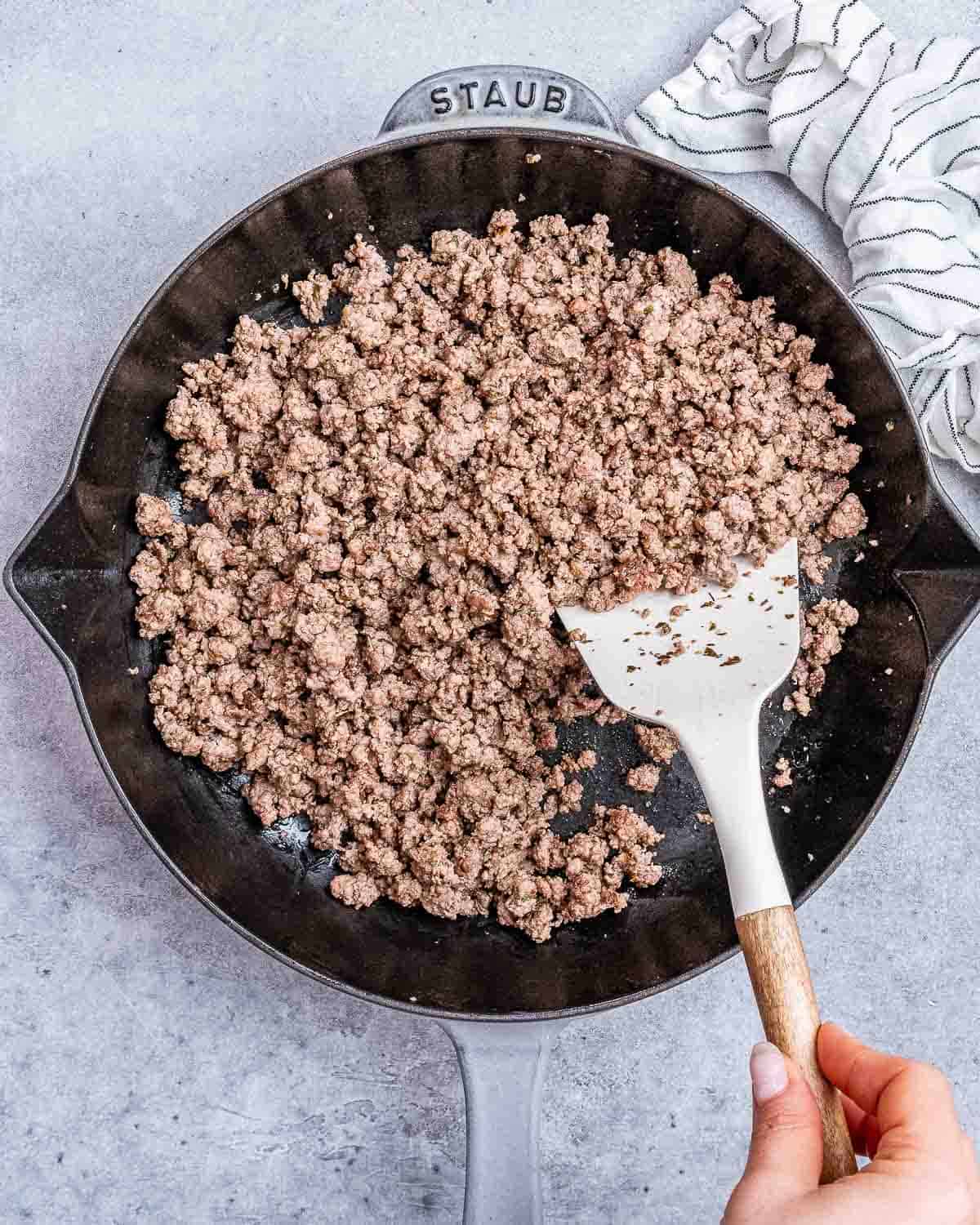 Ground beef in a cast iron skillet stirred by a spatula. 