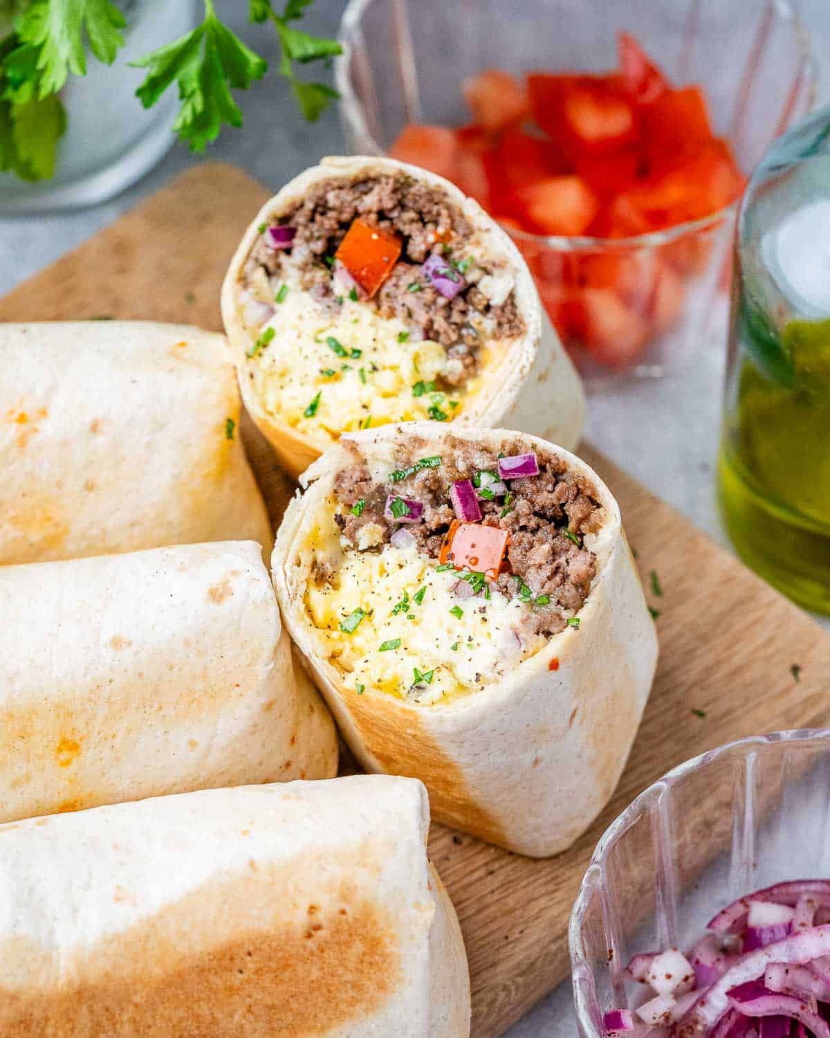 Two halves of burritos standing up showing the ingredients on a wooden cutting board.