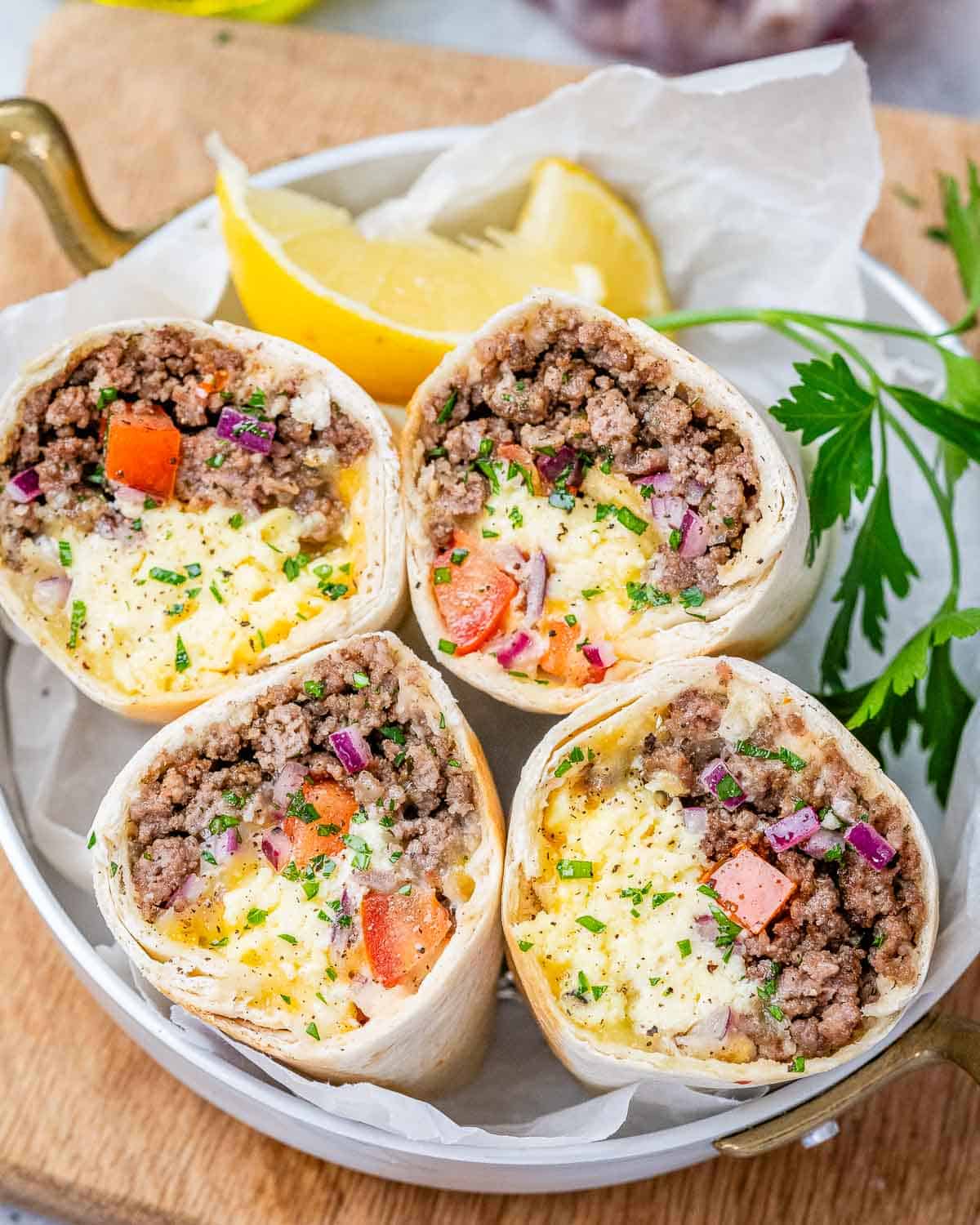 Four halves of a breakfast burrito standing up to show the ingredients on a white plate. 