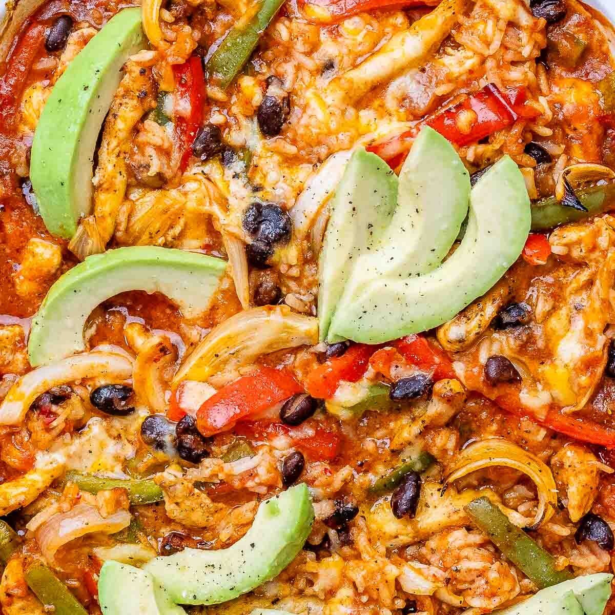 A close up of chicken fajita casserole in a baking dish topped with sliced avocado.