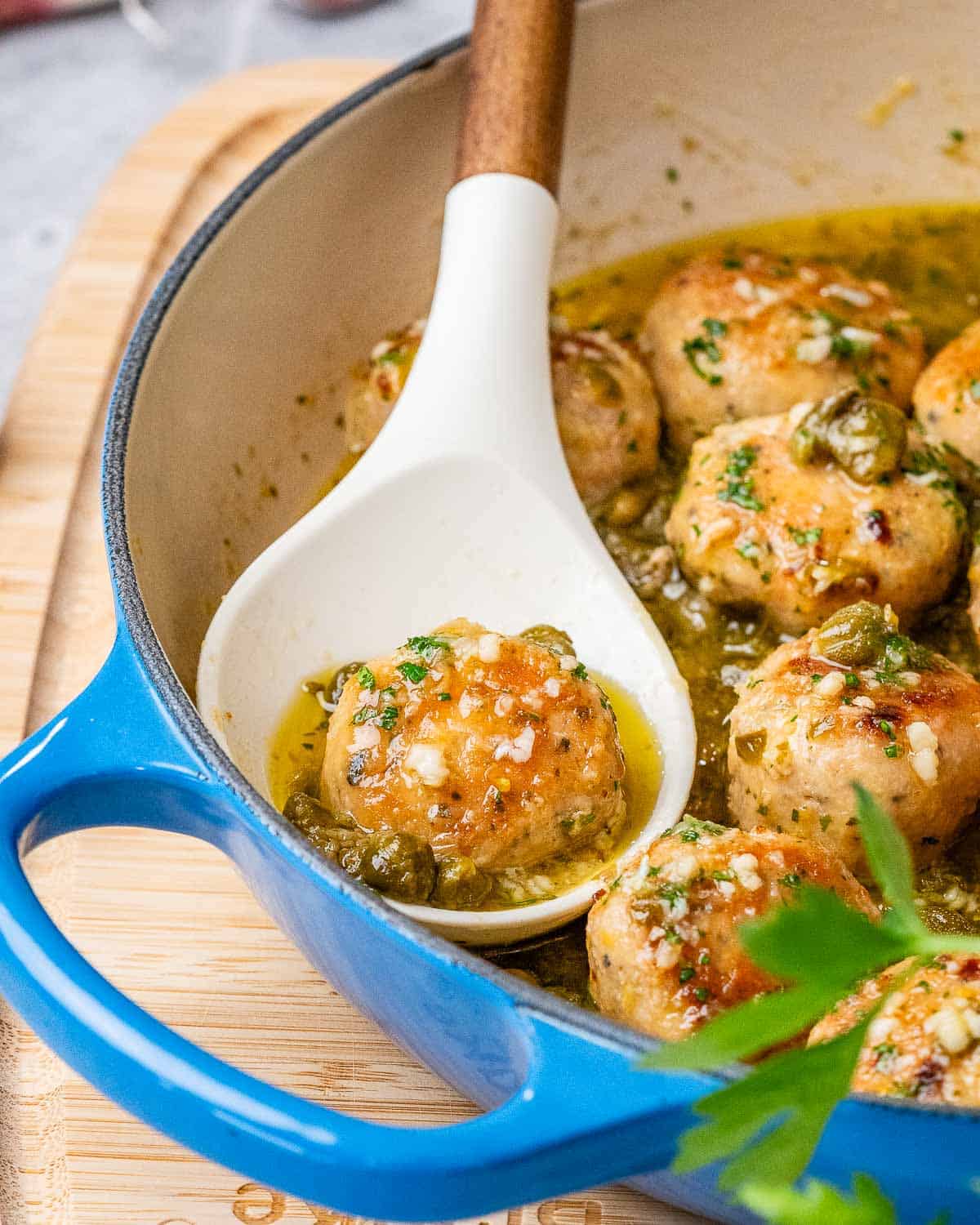 blue skillet with meatballs in it and one meatball on a white spoon.