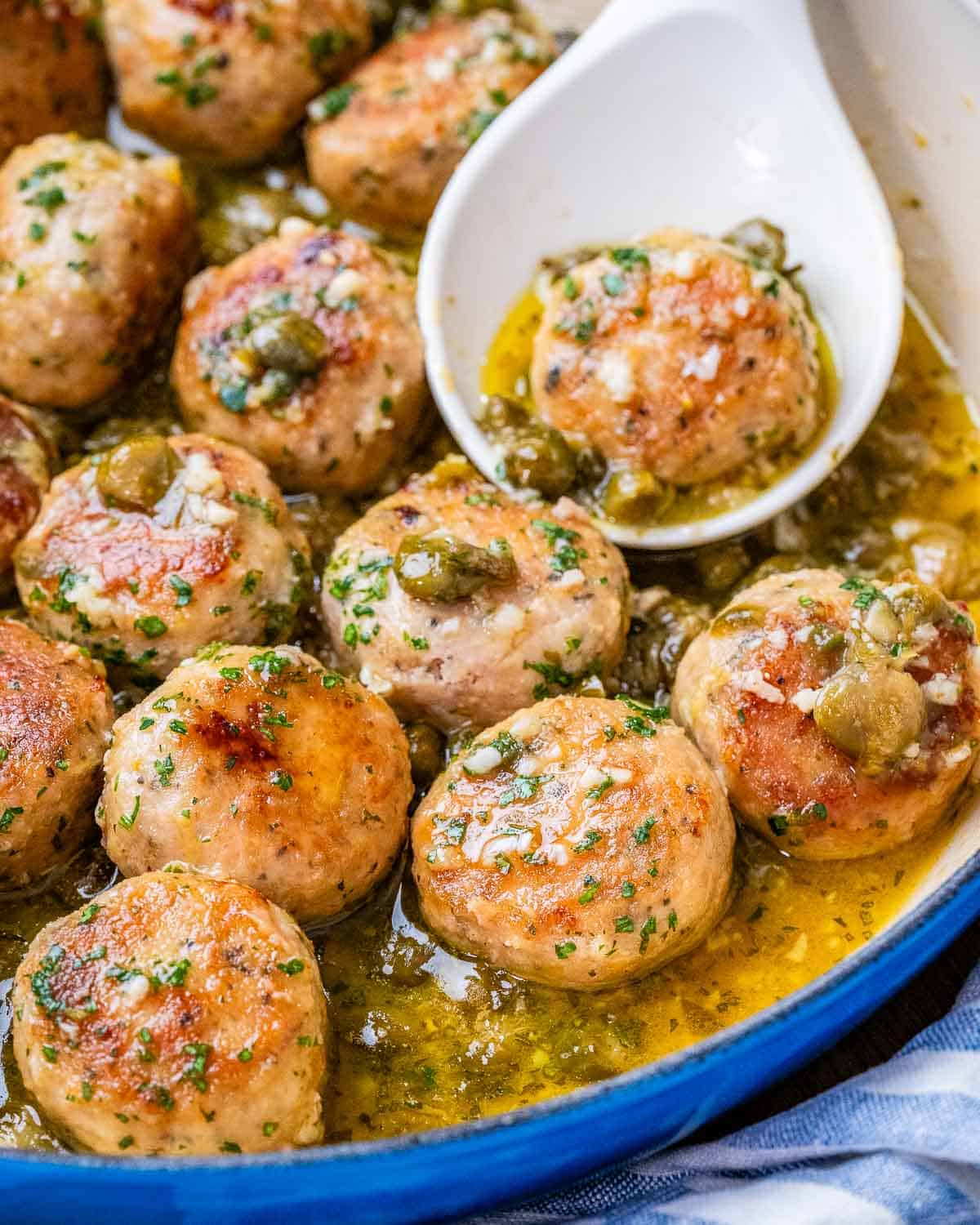 A white spoon holding a meatball in a pot filled with chicken meatballs.