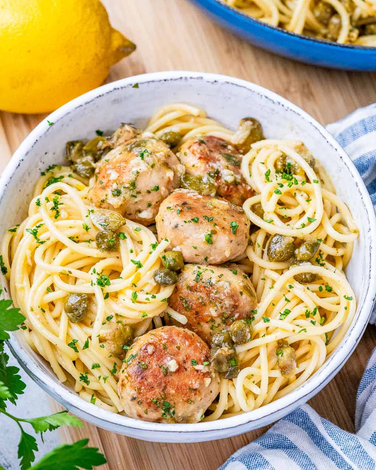 A white bowl filled with spaghetti pasta and topped with chicken meatballs.