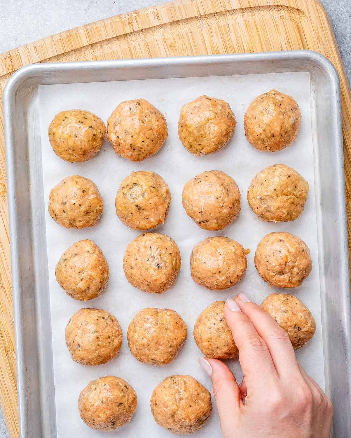 Rolled chicken meatballs on a large baking sheet.