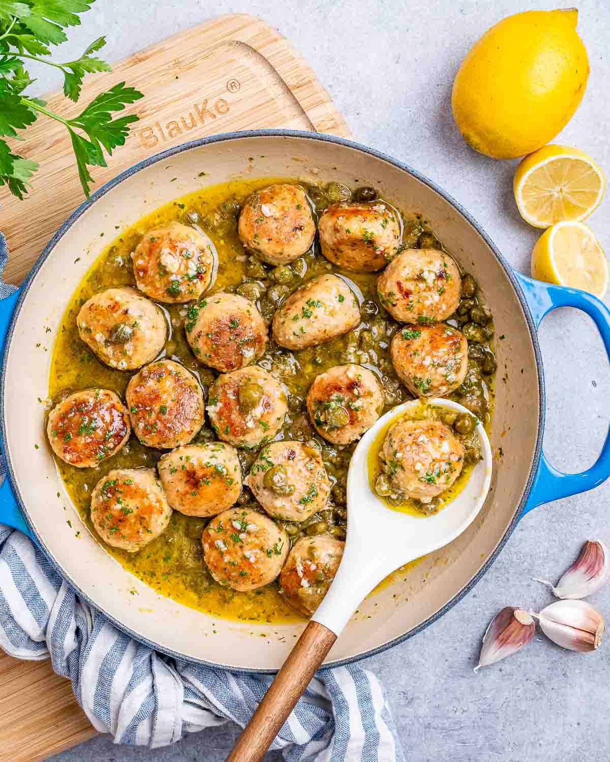 A white spoon holding a meatball in a pot filled with chicken meatballs.