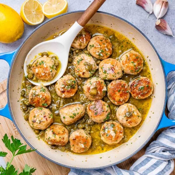 chicken meatballs in a lemony sauces in a skillet with spoon in skillet.