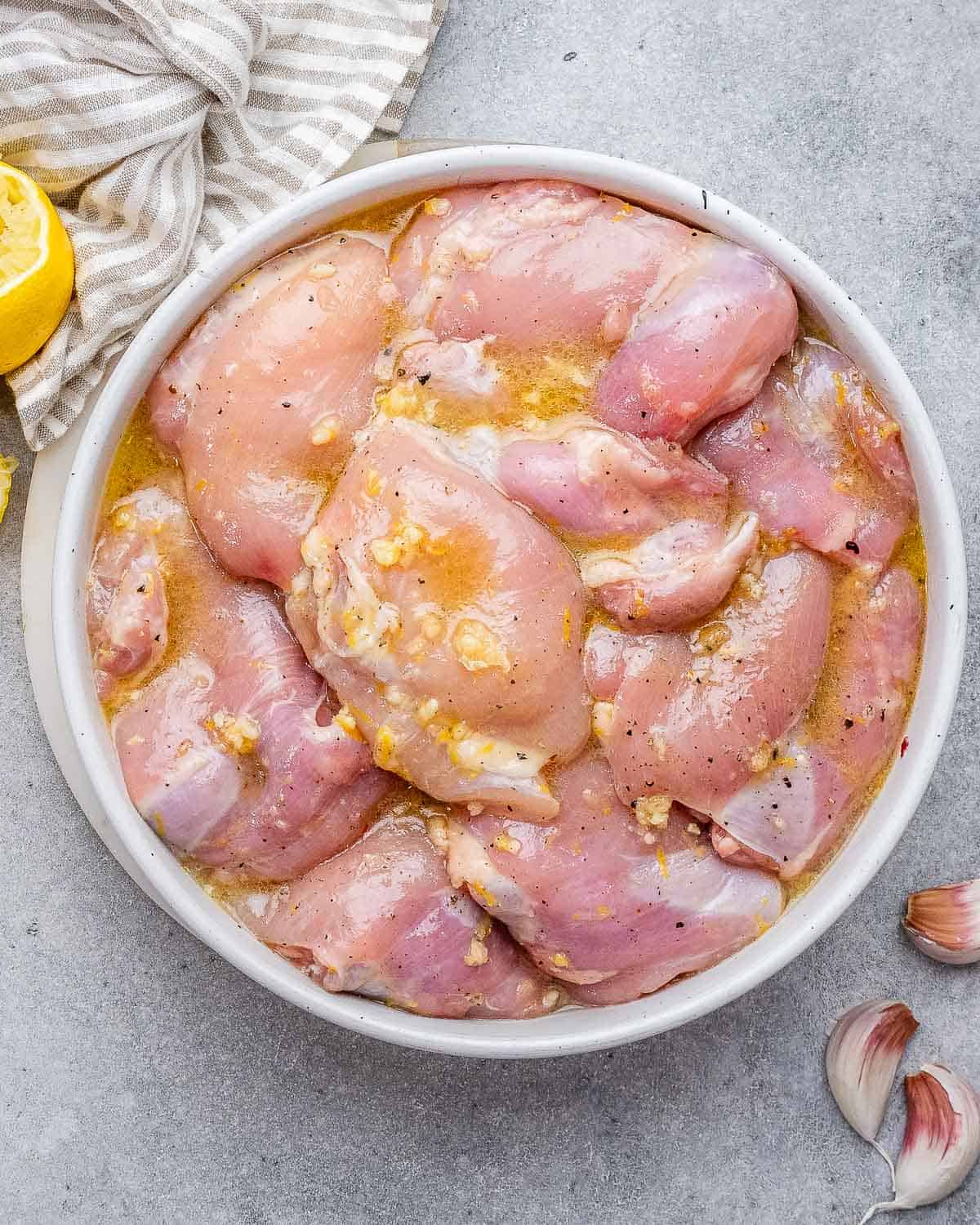 Chicken thighs marinating in a white bowl.