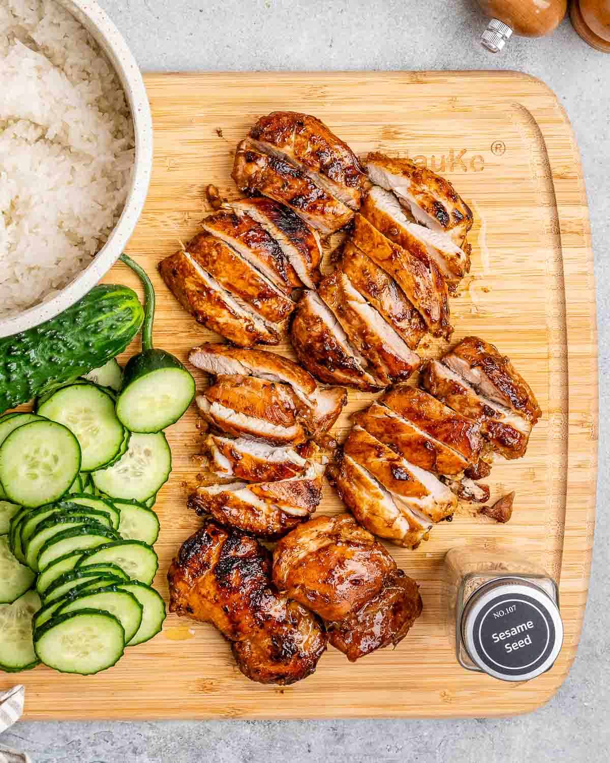 Sliced cooked chicken thighs and cucumbers on a cutting board.